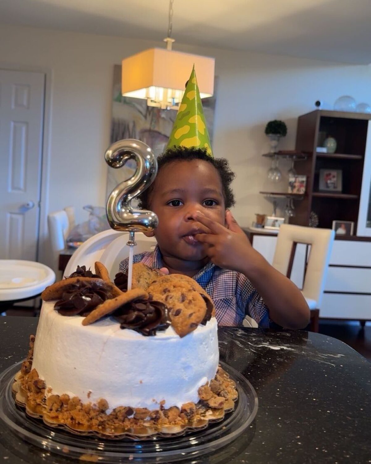 Child in a party hat behind a birthday cake with a number two candle