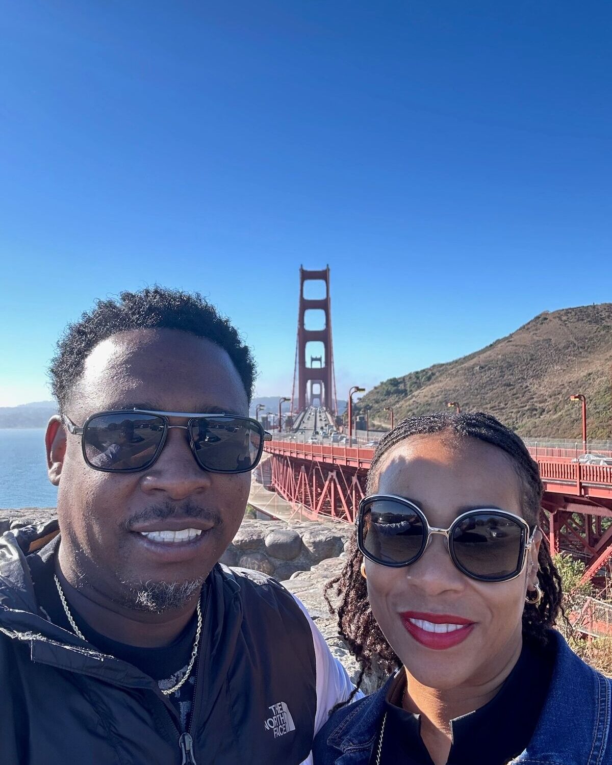 Couple taking a selfie in front of the Golden Gate Bridge under a blue sky