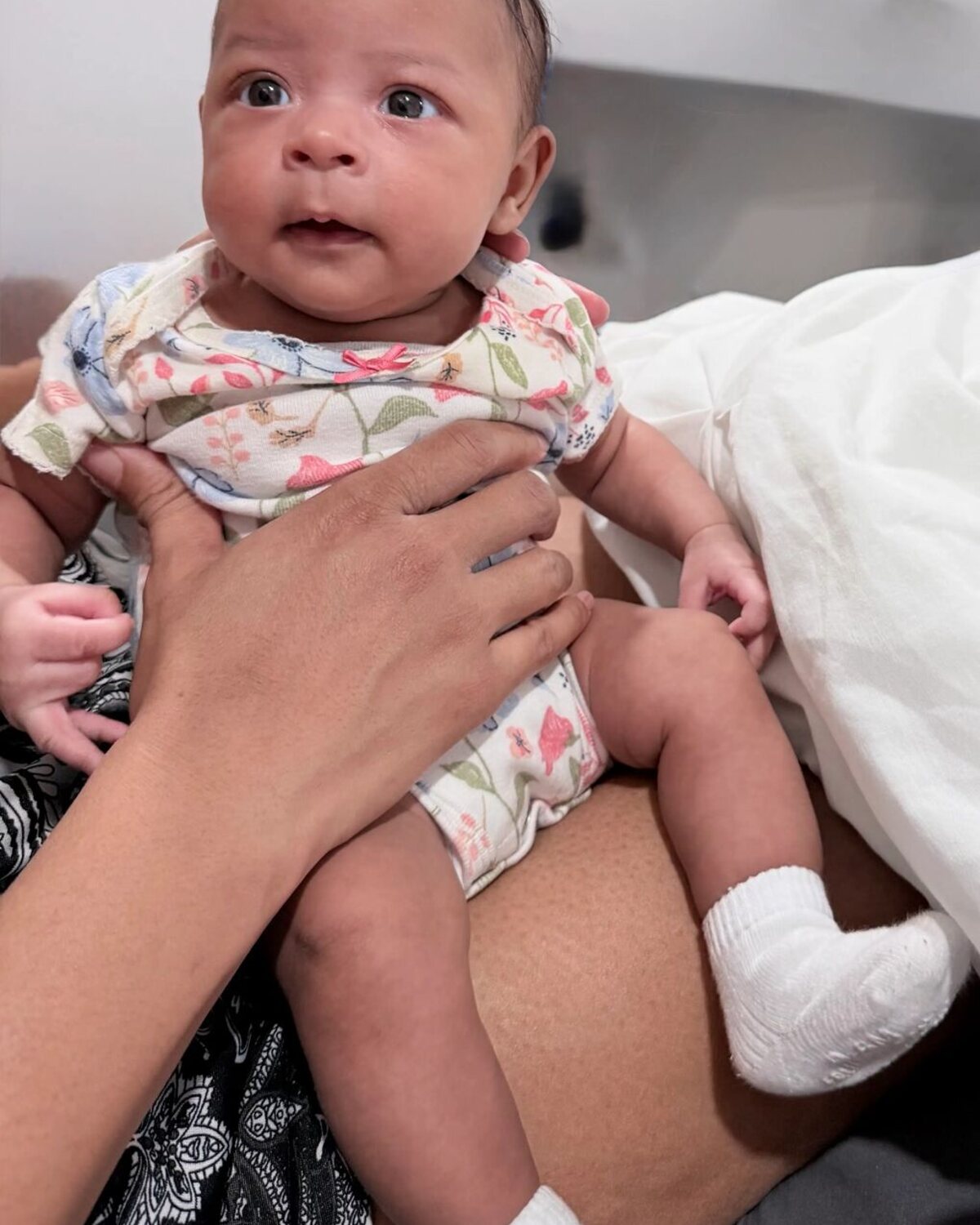 Newborn in a floral onesie resting on an adult lap