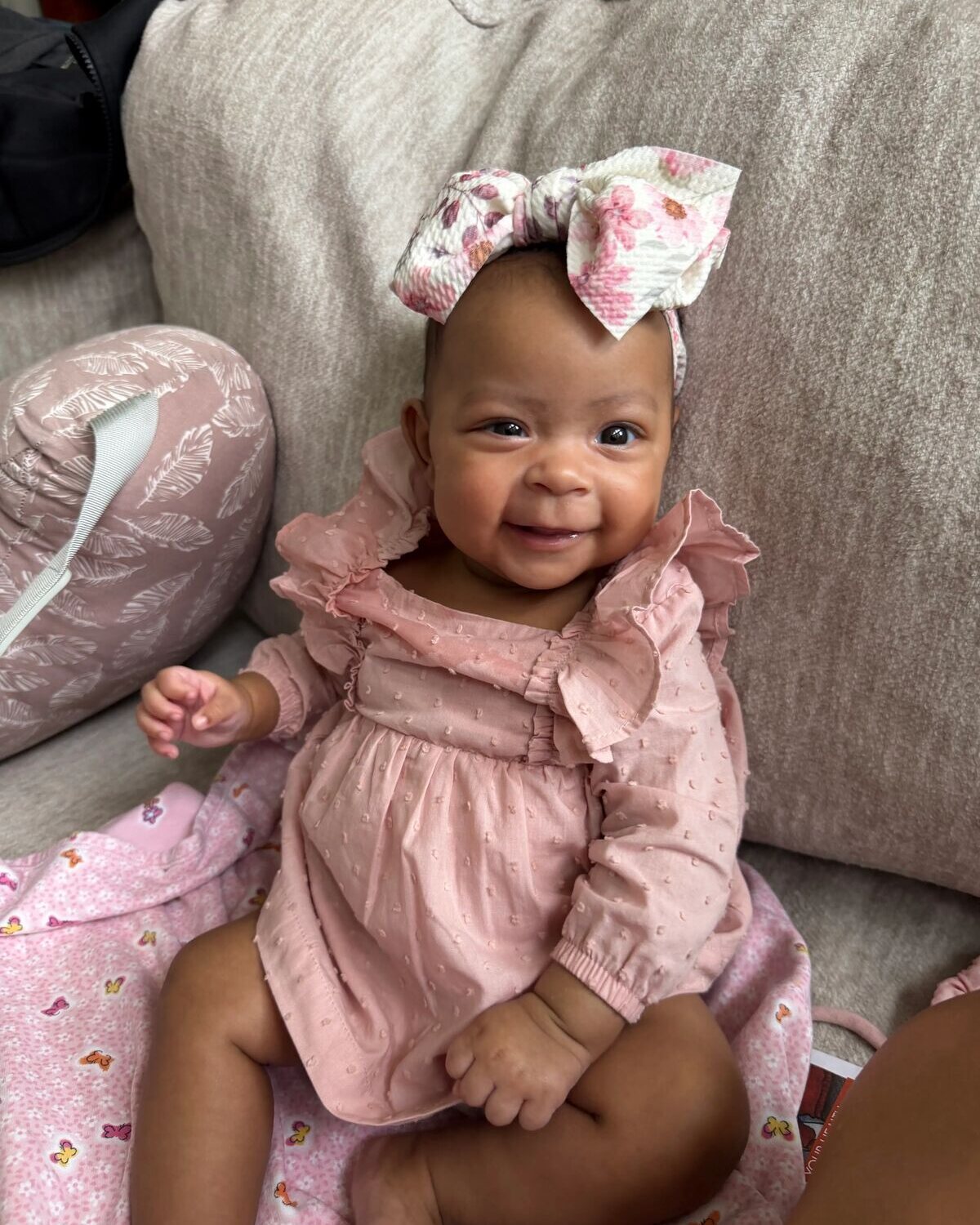Smiling baby in a pink ruffled dress with a floral bow headband