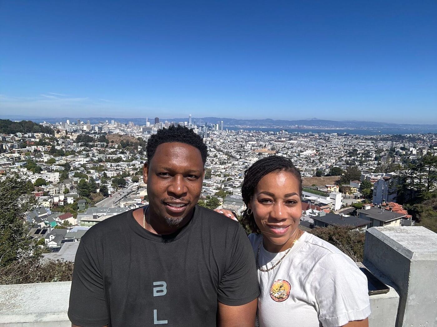 Couple smiling at a lookout with a city skyline and bay behind them