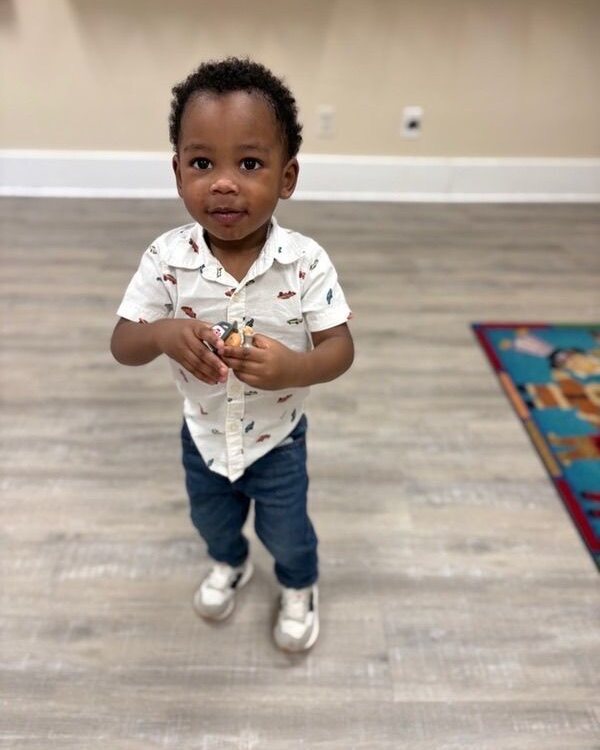 Young boy in a collared shirt and jeans holding a toy indoors